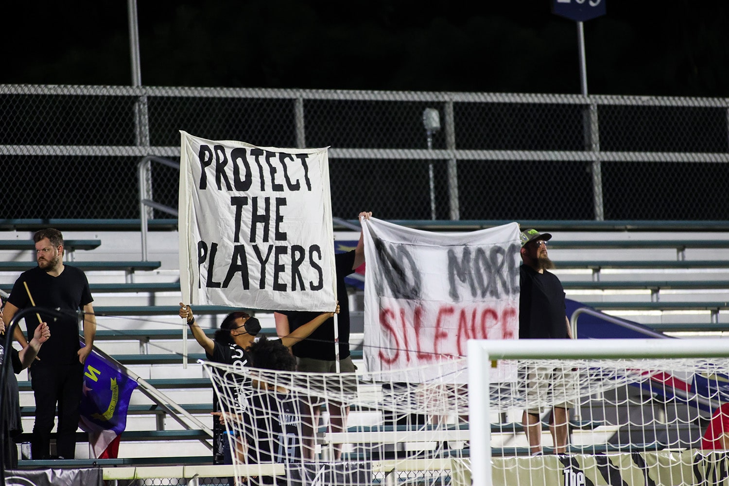 NWSL fans holding signs reading "No more silence" and "respect the players" in response to reports of misconduct by coaches against players