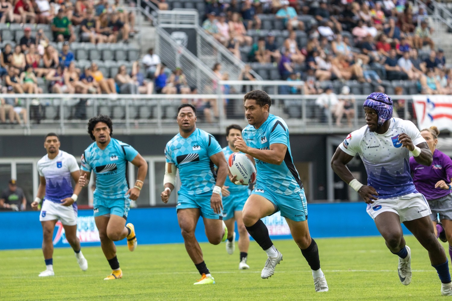 Rugby player in teal jersey escapes from pursuing defender in white jersey