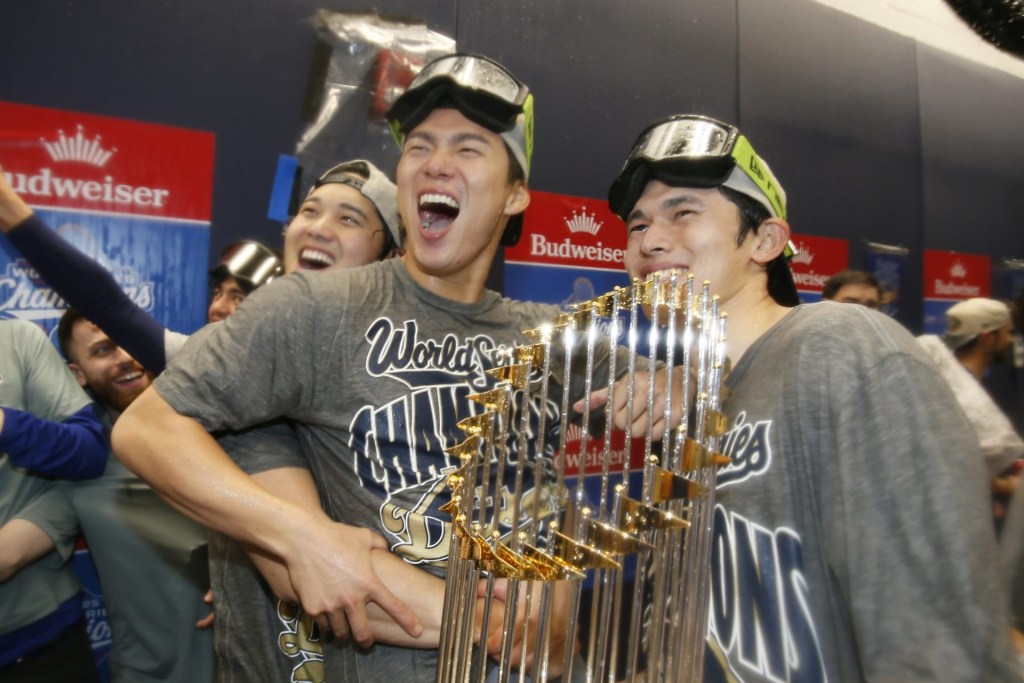 Oct 31, 2025; Toronto, Ontario, CAN; Los Angeles Dodgers two-way player Shohei Ohtani (17) and pitcher Yoshinobu Yamamoto (18) and pitcher Roki Sasaki (11) celebrate with the Commissioner's Trophy in the clubhouse after defeating the Toronto Blue Jays in the 2025 MLB World Series at Rogers Centre.