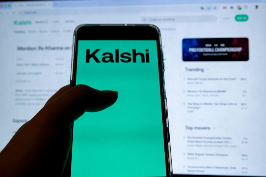 In this photo illustration, a mobile device displays the Kalshi logo while a laptop displays the webpage of the prediction market platform in Copenhagen, Denmark, on February 10, 2026. (Photo by Kristian Tuxen Ladegaard Berg/NurPhoto)