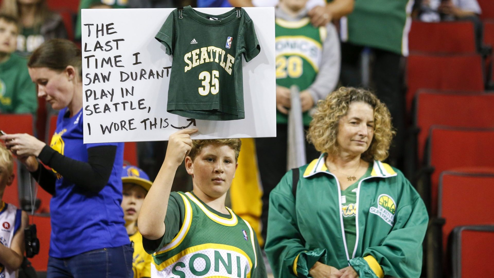Oct 5, 2018; Seattle, WA, USA; Seattle Supersonics fan Ervin Fleshman of Edison, Washington holds a sign with his mother Allison (right) during pregame warmups for a game between the Golden State Warriors and Sacramento Kings at KeyArena.