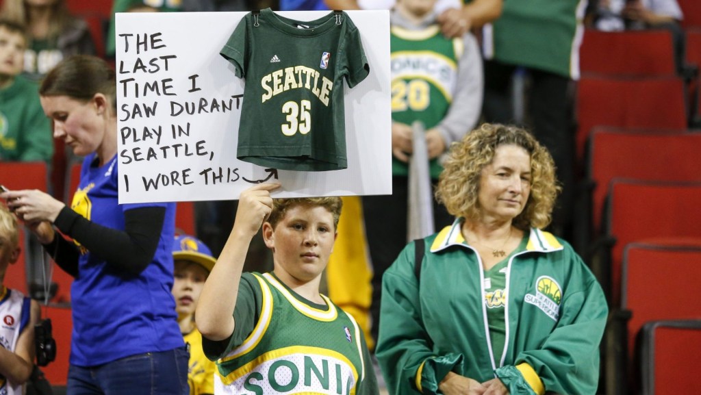 Oct 5, 2018; Seattle, WA, USA; Seattle Supersonics fan Ervin Fleshman of Edison, Washington holds a sign with his mother Allison (right) during pregame warmups for a game between the Golden State Warriors and Sacramento Kings at KeyArena.